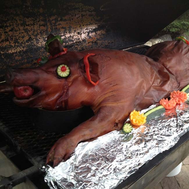 A whole roasted pig on a grill, garnished with veggies—perfect for hog roast catering Watertown MN.