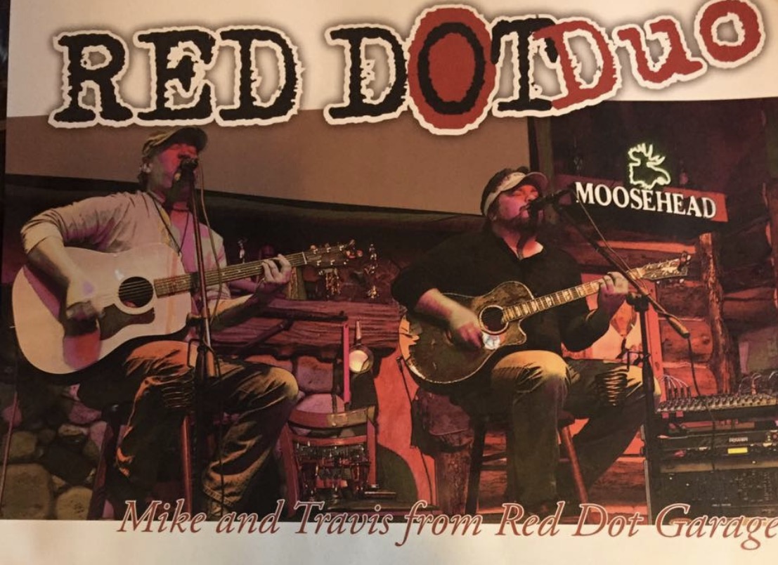 Two men playing guitars and singing on stage under a sign that says Red Dot Duo and Moosehead.